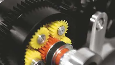 Close-up of a gear assembly: small yellow and orange gears meshing within a larger black gear.