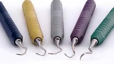 Five dental instruments with colorful, ribbed handles and curved metal tips, arranged in a row.