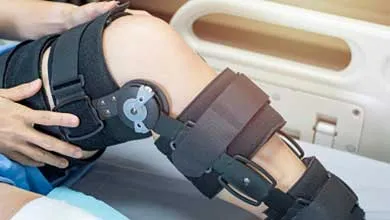 Close-up of a person's leg in a large black hinged knee brace, lying in a hospital bed.