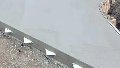Close-up of a smooth, grey concrete sidewalk with white triangular supports along the edge.