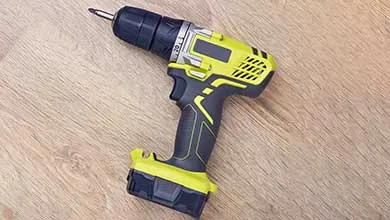 A black and yellow cordless drill with a bit attached, resting on a light wood surface.