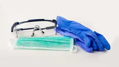 A surgical mask, safety goggles, and blue disposable gloves arranged on a white background.