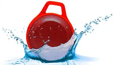 A red circular portable speaker with a handle splashes into clear blue water on a white background.