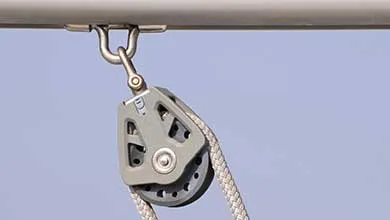A gray pulley with a braided rope threaded through it hangs from a metal bar.
