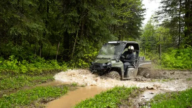 Utility vehicle driving through a shallow stream in a forested environment.