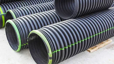 Several large black corrugated plastic pipes stacked horizontally on concrete, with ribbed surfaces, bright green bands around the openings, and green dashed lines along their lengths.