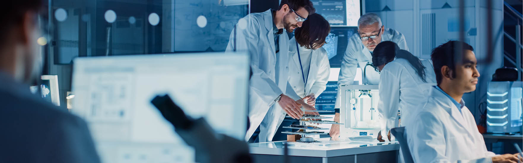 In Technology Research Laboratory: Diverse Team of Industrial Scientists, Engineers, Developers Gather Around Illuminated Table and Inspect Blueprints, Adjust 3D Printer, Choose Component Motherboard